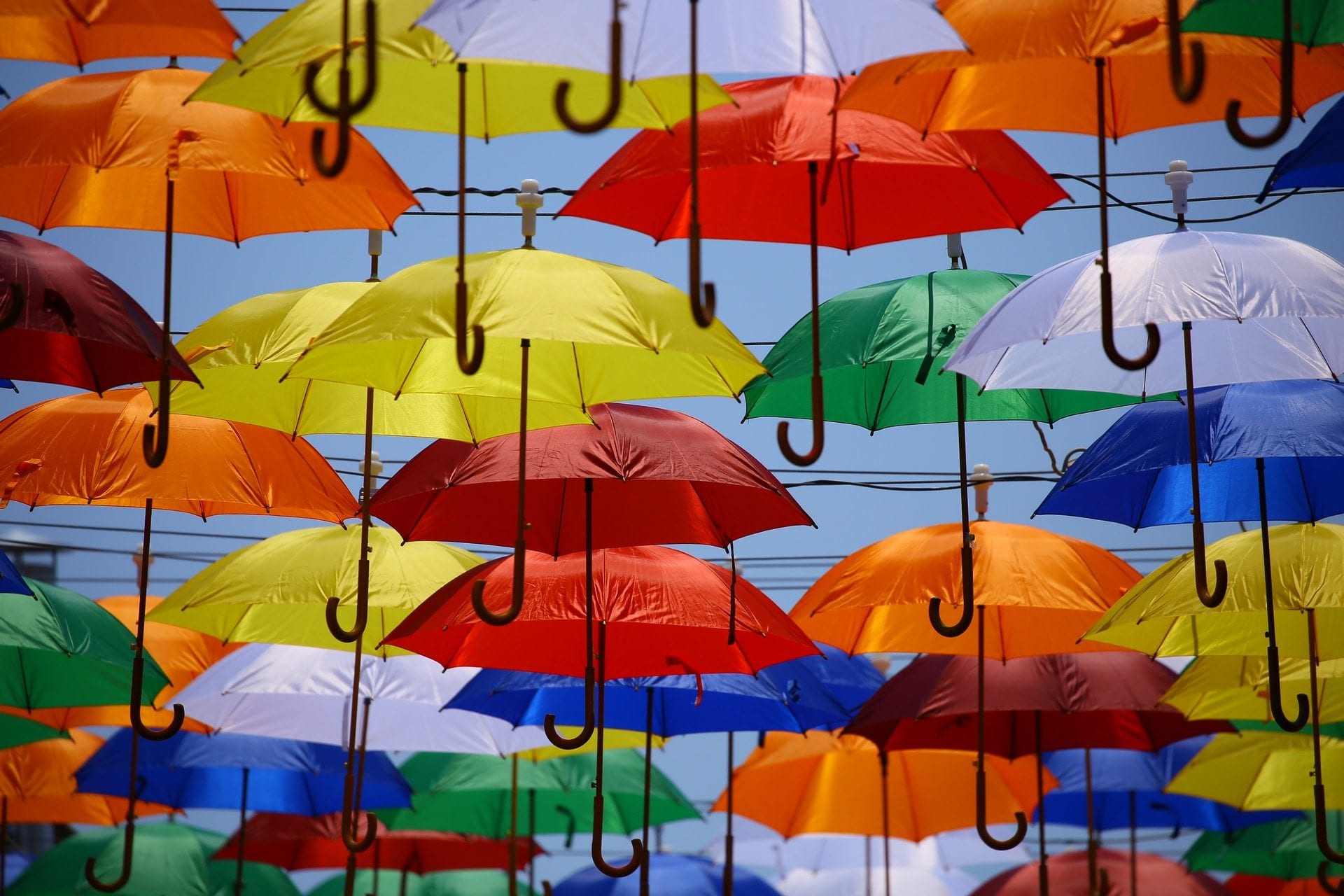 lots of different brightly coloured umbrellas opened against a blue sky