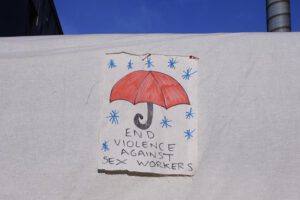 End Violence Against Sex Workers written on a piece of cloth, with a drawing of a red umbrella over it